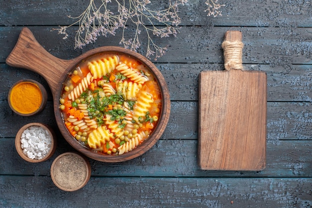 Draufsicht spiralförmige Pastasuppe leckeres Essen mit verschiedenen Gewürzen auf dunkelblauer Schreibtischsuppe Farbe italienische Pastagericht Küche