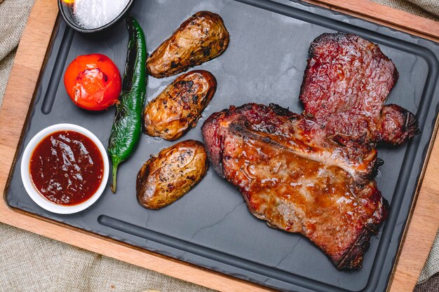Draufsicht Steak in Sauce mit Kartoffeln Tomate und Pfeffer mit Sauce auf einem Tablett
