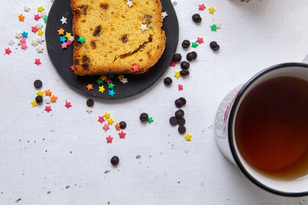 Draufsicht-Stück Kuchen innerhalb dunkler Platte mit bunten Bonbons mit Tee auf dem hellen Hintergrundkuchen süßer Zuckerkeks backen