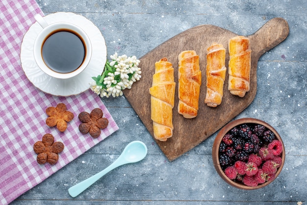 Draufsicht süße köstliche Armreifen mit Füllung zusammen mit Tasse Kaffee Kekse Beeren auf dem grauen hölzernen Schreibtisch süß backen Gebäck Keks Keks