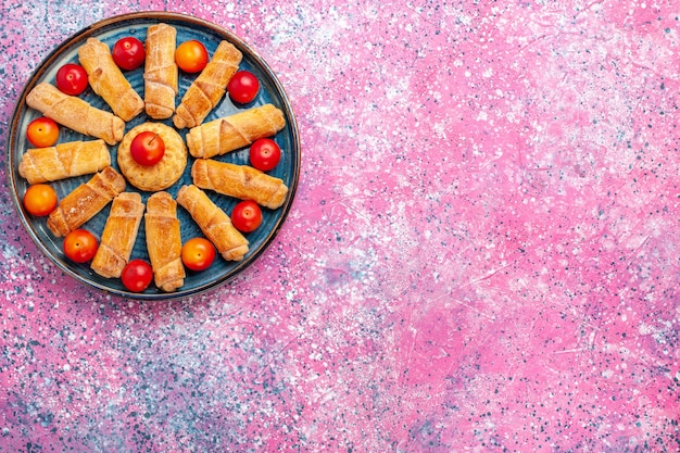 Draufsicht süße köstliche Bagels gebackenes Gebäck innerhalb Tablett mit Pflaumen auf dem rosa Schreibtisch