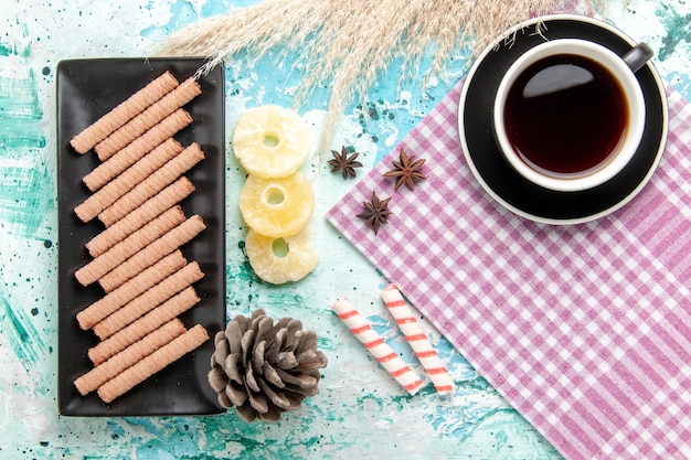 Draufsicht süße lange Kekse mit Tasse Tee und getrockneten Ananasringen auf dem blauen Hintergrund