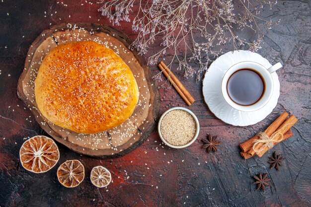 Draufsicht süßes gebackenes Brötchen mit Tasse Tee auf der dunklen Oberfläche