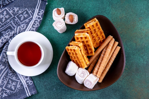 Draufsicht Süßigkeiten Waffeln süße Brötchen und Marmelade mit einer Tasse Tee auf Grün