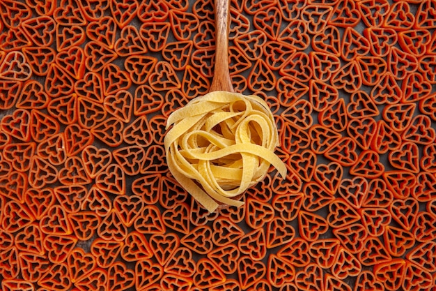 Kostenloses Foto draufsicht tagliatelle auf löffel auf rote herzen italienische pasta auf dunklem tisch