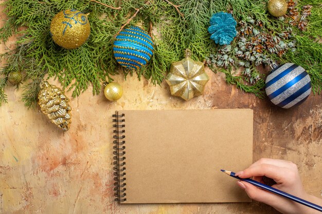 Draufsicht tannenzweige weihnachtsbaum ornamente notebook stift in der hand der frau auf beige hintergrund