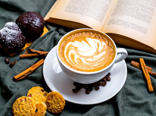 Draufsicht Tasse Cappuccino mit Schokoladenplätzchen und Rosinenplätzchen und mit einem Buch auf dem Tisch