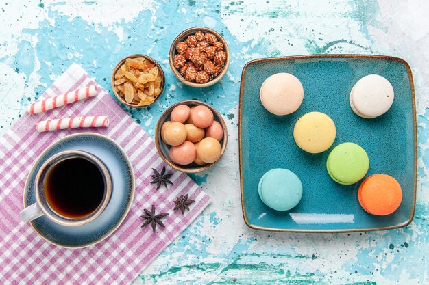 Draufsicht Tasse Kaffee mit französischen Macarons Rosinen und Confitures auf hellblauem Oberflächenkuchen backen süßen Zuckerkuchenplätzchen