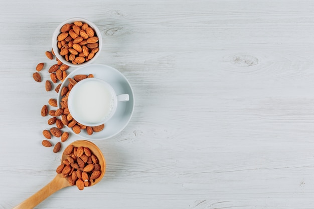 Draufsicht tasse milch mit mandeln in holzlöffeln auf weißem holzhintergrund. horizontaler freier speicherplatz für ihren text