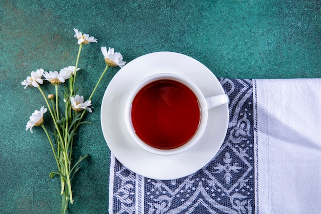 Draufsicht Tasse Tee auf Küchentuch mit Gänseblümchen auf Grün