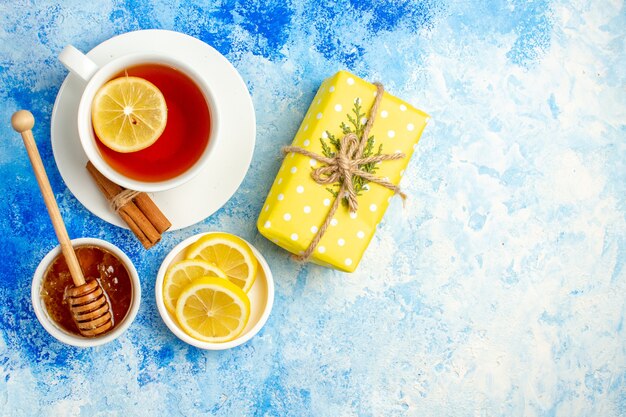 Draufsicht Tasse Tee gelbe Geschenkbox Zitronenscheiben Honig auf blauem Tisch Freiraum