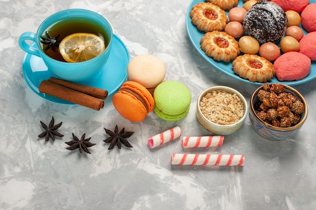 Kostenloses Foto draufsicht tasse tee mit französischen macarons keksen und kuchen auf weißer oberfläche