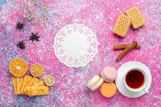 Draufsicht Tasse Tee mit französischen Macarons und Crackern auf dem hellrosa Schreibtisch