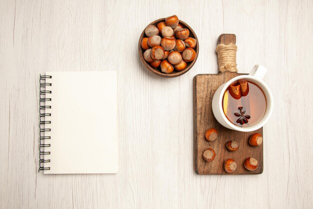 Draufsicht Tasse Tee mit frischen Haselnüssen auf weißem Schreibtisch Teenuss Snack Zeremonie Haselnuss