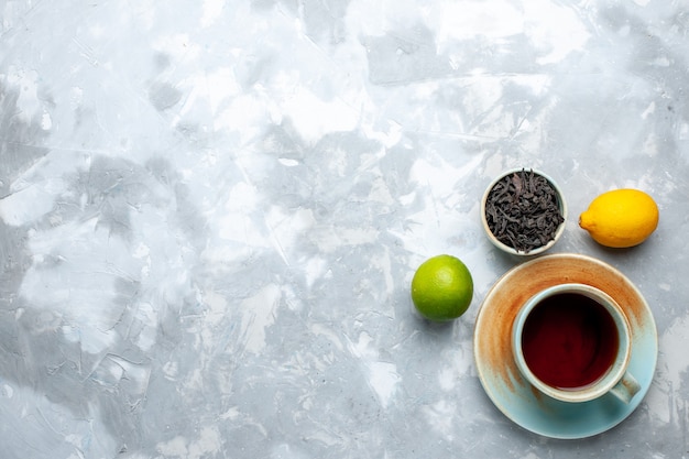 Draufsicht Tasse Tee mit frischen Zitronen und getrocknetem Tee auf dem Leuchttisch, Tee Frucht Zitrusfarbe Getränk