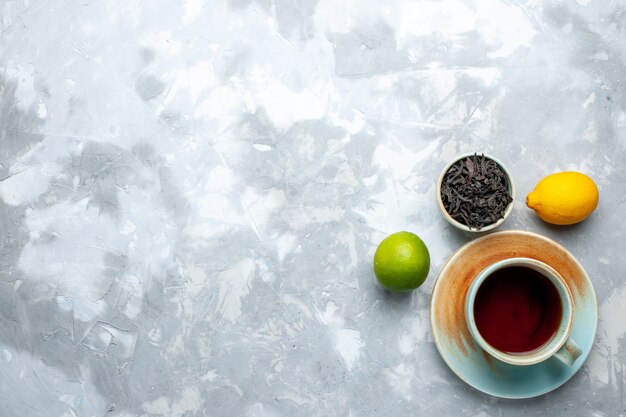 Draufsicht Tasse Tee mit frischen Zitronen und getrocknetem Tee auf dem Leuchttisch, Tee Frucht Zitrusfarbe Getränk