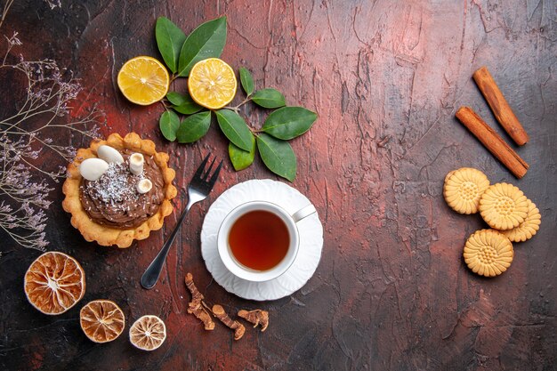 Draufsicht Tasse Tee mit köstlichem kleinen Kuchen auf dunklem Tisch, Dessertkeksplätzchen