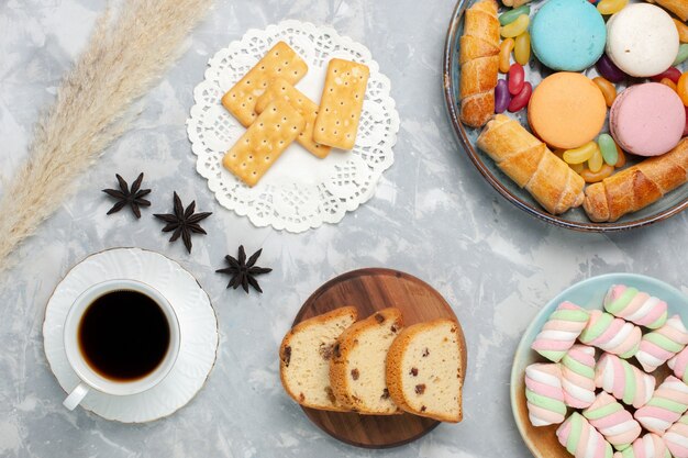 Draufsicht Tasse Tee mit Kuchen Bagels und Macarons auf Weiß