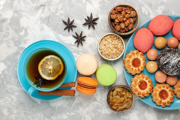 Draufsicht tasse tee mit macarons und rosinen auf dem weißen schreibtisch