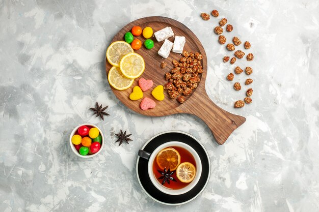 Draufsicht Tasse Tee mit Nüssen und Bonbons auf weißem Wandbonbon Zucker süßer Kekskuchen Tee