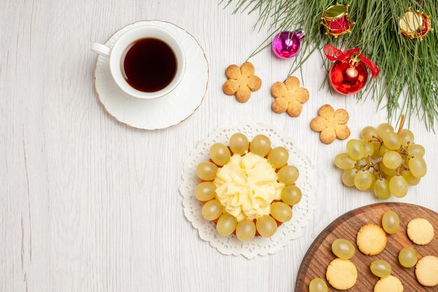 Draufsicht Tasse Tee mit Sahnetorte und Trauben auf weißem Schreibtisch Früchtetee Dessert Sahne Kekskuchen