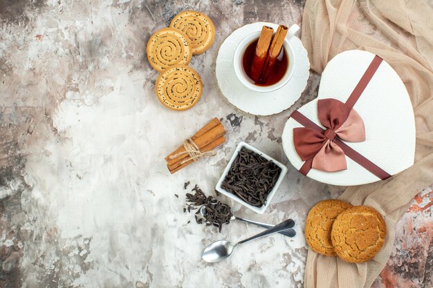 Draufsicht Tasse Tee mit süßen Keksen und Geschenk auf hellem Hintergrund Zeremonie Break Pie Kaffee Zuckerkeks Zimtfarbe