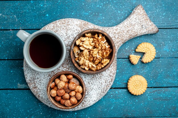 Draufsicht-Tasse Tee mit Walnüssen und Haselnüssen auf blauer rustikaler Schreibtischnuss-Snack-Teefarbe