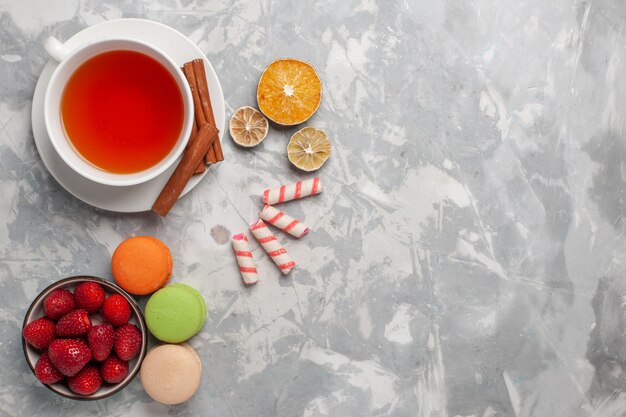 Draufsicht Tasse Tee mit Zimt und französischen Macarons auf weißem Schreibtisch