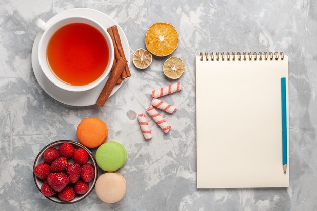 Draufsicht Tasse Tee mit Zimt und französischen Macarons auf weißer Oberfläche