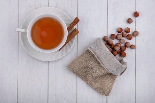 Draufsicht Tasse Tee mit Zimt und Haselnüssen in einem Leinensack auf grauem Hintergrund