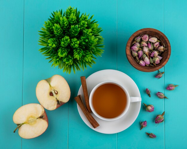 Draufsicht-Tasse Tee mit zimtgrünem Apfel und trockenen Rosenknospen auf einem blauen Hintergrund