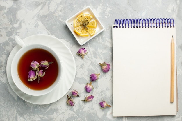 Draufsicht Tasse Tee mit Zitrone und Notizblock auf weißem Schreibtisch