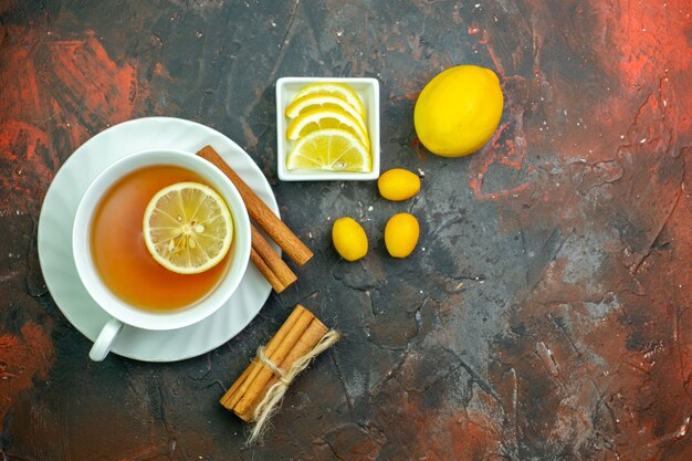 Draufsicht Tasse Tee mit Zitronen-Cumcuat-Zitronenscheiben in kleinen Schüssel-Zimt auf dunkelrotem Hintergrund gewürzt