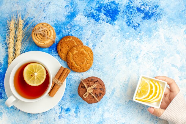 Draufsicht Tasse Teeplätzchen Zitronenscheiben in Schüssel in Frauenhand auf blauem Tisch Freiraum