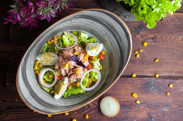 Draufsicht Thunfischsalat mit Salat, Tomaten, Eiern, Gurke, Zwiebel und Mais auf einer dunklen Holzoberfläche horizontal_