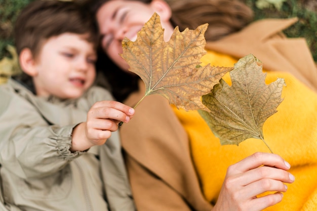 Draufsicht unkonzentrierter kleiner Junge und Mutter, die mit Herbstlaub spielen