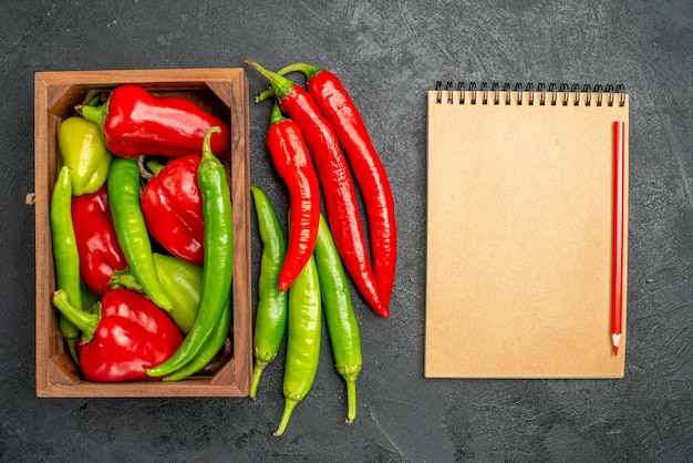 Draufsicht verschiedene Arten von Paprika in der Box in der Nähe von Notebook und rotem Stift auf schwarzer Oberfläche mit freiem Platz