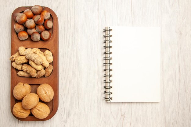 Draufsicht verschiedene frische Nüsse Erdnüsse Haselnüsse und Walnüsse auf weißem Schreibtisch Nuss Snack viele Pflanzen