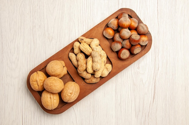 Draufsicht verschiedene frische Nüsse Erdnüsse Haselnüsse und Walnüsse auf weißem Schreibtisch Nuss Snack viele Pflanzen