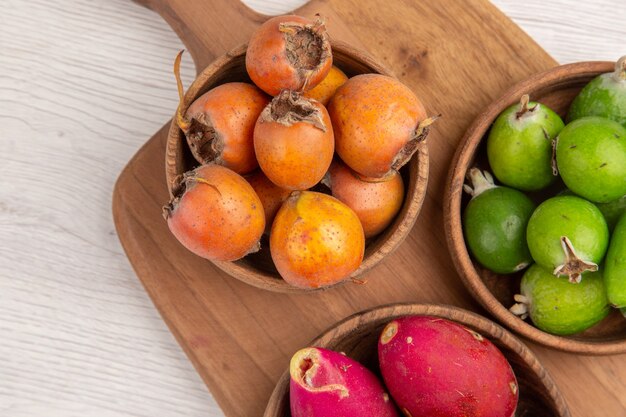 Draufsicht verschiedene Früchte Feijoas Beeren und andere Früchte in Tellern auf weißem Hintergrund reifes Essen exotische Farbe