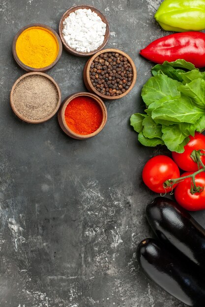 Draufsicht verschiedene Gewürze in kleinen Schüsseln Tomaten Paprika Auberginen Grüns auf grauem Hintergrund