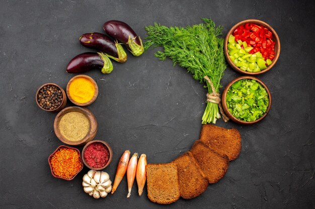 Draufsicht verschiedene Gewürze mit Grüns und dunklen Brotlaiben auf dunklem Hintergrund Salatgewürze Brotmahlzeit Gesundheit