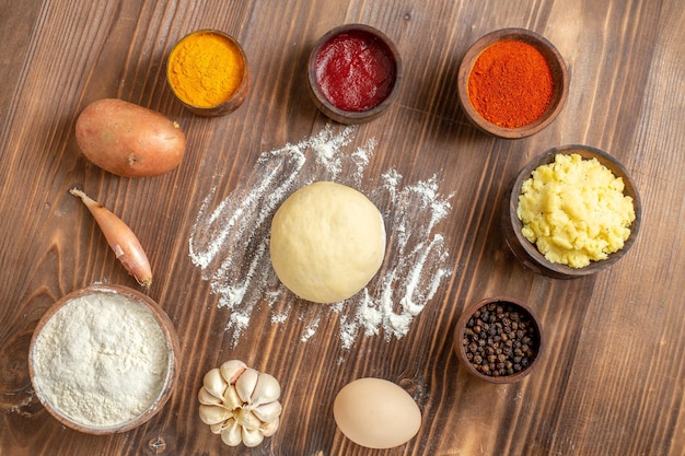 Kostenloses Foto draufsicht verschiedene gewürze mit kartoffelpüree und knoblauch auf dem braunen holzschreibtisch würziges pfeffer reifes kartoffelessen