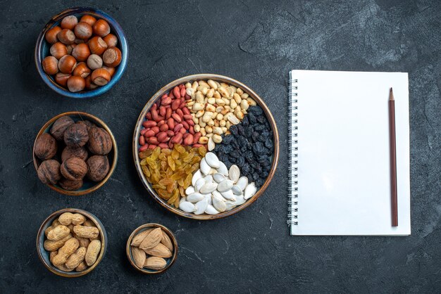 Draufsicht verschiedene Nüsse mit Rosinen und getrockneten Früchten auf der dunkelgrauen Hintergrundnuss-Snack-Haselnuss-Walnuss-Erdnuss