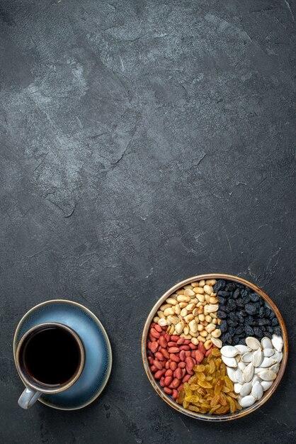 Draufsicht verschiedene Nüsse mit Rosinen und Tasse Kaffee auf der dunkelgrauen Hintergrundnuss-Snack-Walnuss-Erdnuss