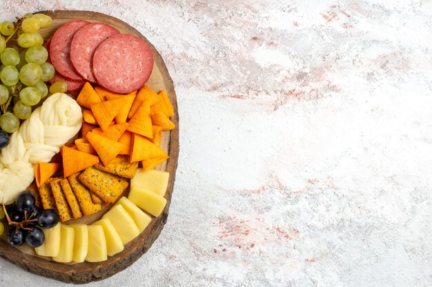 Draufsicht verschiedene Snacks Cips Würstchen Käse und frische Trauben auf dem hellen weißen Raum