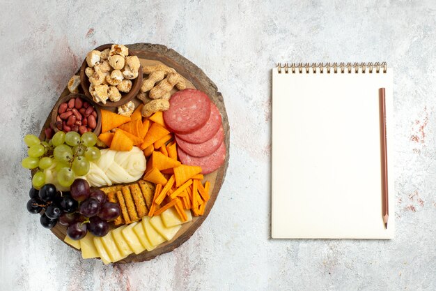 Draufsicht verschiedene Snacks Nüsse Cips Trauben Käse und Würstchen auf dem weißen Hintergrund Nuss Snack Mahlzeit Lebensmittel Früchte
