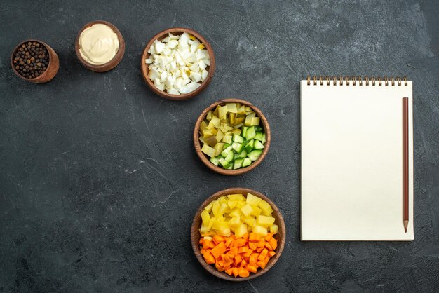 Draufsicht verschiedener Salatzutaten mit Notizblock auf dem grauen Oberflächensalat-Gemüsemahlzeitsnack