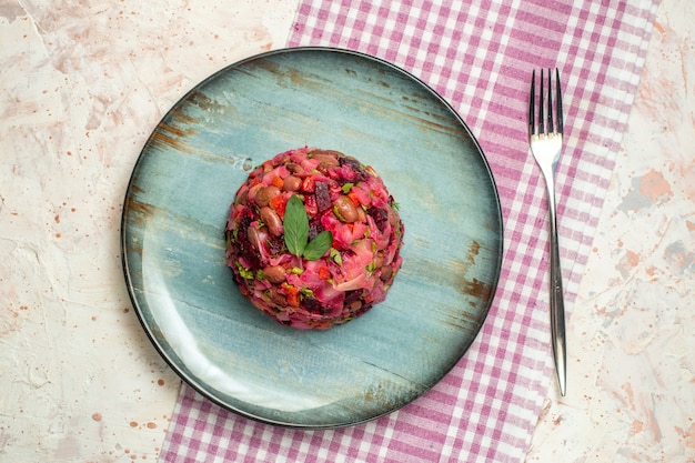 Draufsicht-Vinaigrette-Salat auf ovalem Teller und Gabel auf weiß-violett karierter Tischdecke auf hellgrauem Tisch