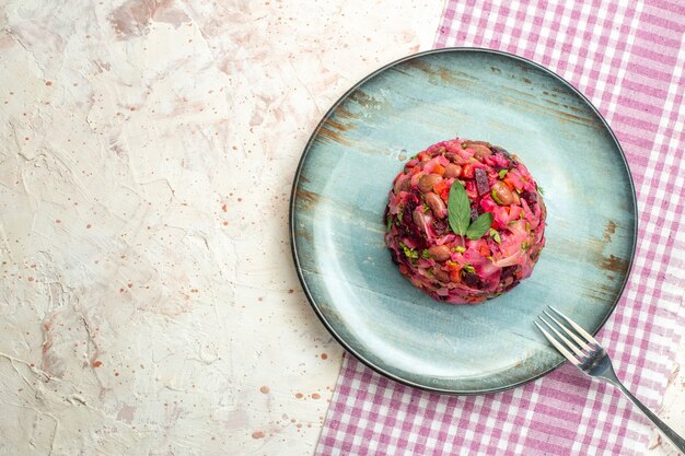 Draufsicht-Vinaigrette-Salatgabel auf ovalem Teller auf weiß-violett karierter Tischdecke auf hellgrauem Tischkopierplatz